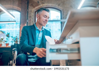 Smiling Man In Wheelchair Putting Papers In Desk Drawer