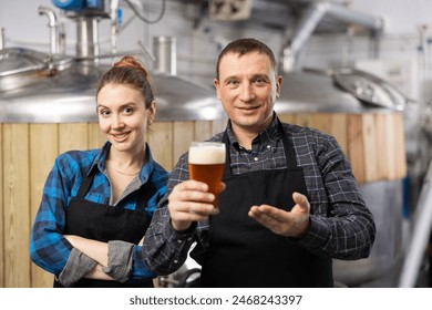 Smiling man and woman brewers presenting new beer in beer factory. Woman making thumb up gesture. - Powered by Shutterstock