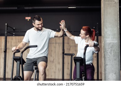 Smiling man and woman doing intensive workout together by pedaling air bike and high five in modern gym. Healthy lifestyle - Shutterstock ID 2170751659