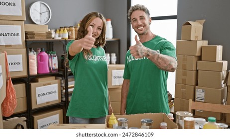 Smiling man and woman in green volunteer shirts giving thumbs up in a donation center with boxes - Powered by Shutterstock