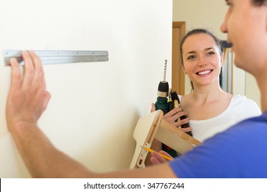 Smiling Man And Woman Hanging Shelf On The Wall At Home
