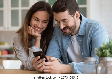 Smiling Man And Woman Looking At Smartphone Screen Together, Young Couple Watching Funny Video, Chatting In Social Network Together, Reading Good News In Message, Playing Game, Shopping Online