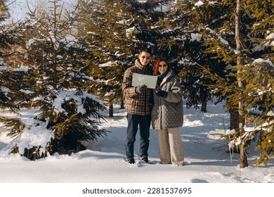 Smiling man and woman stand in the middle of the forest with a map in their hands. A young couple spends a day off in nature.