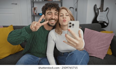 Smiling man and woman taking a selfie, making peace sign and blowing kiss in a cozy living room. - Powered by Shutterstock