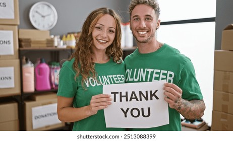 A smiling man and woman volunteers holding a 'thank you' sign in a donation center warehouse. - Powered by Shutterstock