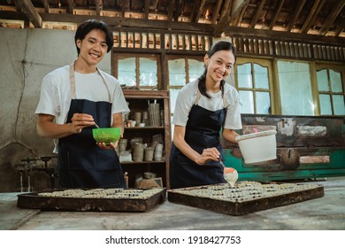 smiling man and woman wearing an apron looking at the camera while stirring the cake dough in a bowl near the cake tin on the table. - Powered by Shutterstock