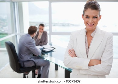 Smiling Marketing Manager Standing In Conference Room With Team Sitting Behind Her