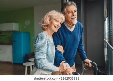 Smiling married senior couple standing in front of the window looking out at the view - Powered by Shutterstock