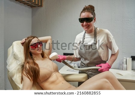 a smiling master holds a laser maniple in his hands and removes hair in the armpit of a woman. laser hair and tattoo removal. laser rejuvenation