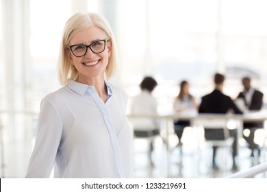 Smiling mature attractive businesswoman in glasses looking in camera, happy friendly middle aged female executive, older team leader or business coach mentor posing in office, headshot portrait