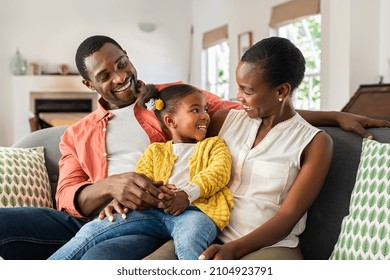 Smiling Mature Black Family Relaxing On Couch. Happy Middle Aged Man And Beautiful Woman Sitting On Sofa At Home With Daughter While Talking Together. Happy African Father And Mother With One Girl.