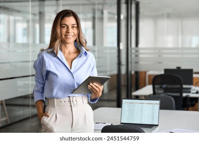 Smiling mature business woman manager executive, happy middle aged businesswoman entrepreneur, 40 year old professional hr holding digital tablet looking at camera standing in office at work. Portrait - Powered by Shutterstock