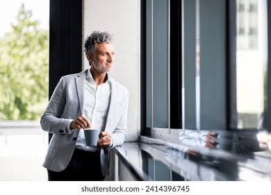 Smiling mature businessman with coffee mug looking out of window - Powered by Shutterstock