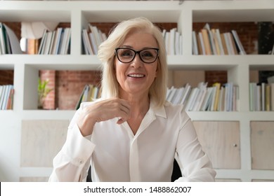 Smiling mature businesswoman sit at desk in office talk with client customer have conversation on webcam, happy positive middle-aged female employee in glasses video call at workplace