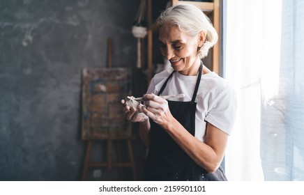 Smiling mature caucasian female sculptor making ceramic pottery with wooden stick. Small business and entrepreneurship. Home hobby, entertainment and leisure. Art studio. Woman wearing work apron - Powered by Shutterstock