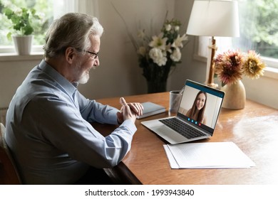 Smiling Mature Caucasian Man Sit At Desk Talk Speak On Video Call On Computer With Adult Daughter. Happy Old 70s Male Have Webcam Digital Virtual Event On Laptop With Colleague. Communication Concept.