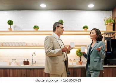 Smiling mature colleagues actively gesturing when talking and drinking coffee in office kitchen