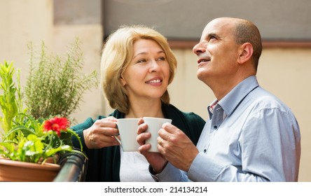 Smiling mature couple discussing and drinking tea at balcony - Powered by Shutterstock