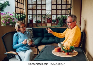 Smiling mature couple having a conversation in the morning while drinking coffee at balcony or terrace. Elderly people love concept. Enjoyment of retirement. Copy space. - Powered by Shutterstock