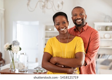 Smiling mature couple holding each other at home. Loving african couple standing in living room embracing and looking at camera. Husband hugging wife from stomach at new apartment with copy space.