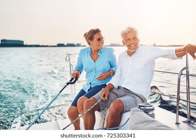 Smiling mature couple sitting together on the deck of their boat while out for a sail on a sunny afternoon