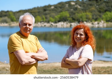 Smiling mature couple standing confidently by a serene lake, surrounded by lush greenery and distant hills, embracing nature's tranquility - Powered by Shutterstock