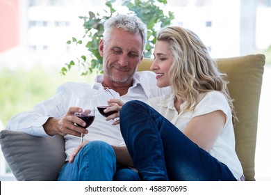 Smiling Mature Couple Toasting Red Wine While Sitting At Home