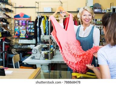 Smiling Mature Employee Returning Dress To Customer In Sewing Studio