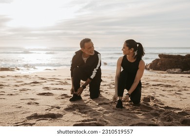 Smiling mature european man and woman tying shoelaces for start to jogging, enjoy workout together in morning on sea beach, outdoor. Weight loss, sports, fitness and body care - Shutterstock ID 2310519557