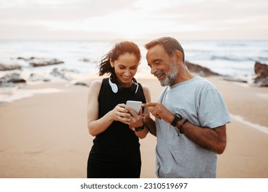 Smiling mature european woman and man in sportswear rest from workout together with smartphone in morning on sea beach, outdoor. App, sports blog, fitness and body care, social networks - Shutterstock ID 2310519697