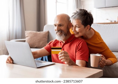 Smiling mature family couple holding bank credit card and looking at laptop screen, elderly spouses entering payment information, enjoying fast money transfer service or online shopping at home - Powered by Shutterstock