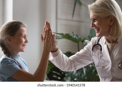 Smiling Mature Female Doctor Or Nurse Give High Five To Happy Teen Girl Child After Checkup In Hospital. Happy Woman Pediatrician Make Deal With Small Kid Patient In Clinic. Healthcare Concept.