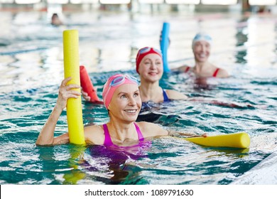 Smiling mature female in swimwear and two more active women listening to trainer advice during gymnastics in water