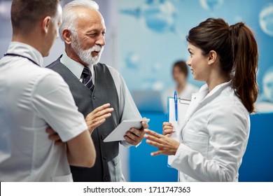 Smiling mature financial advisor and doctors communicating while standing in a lobby at medical clinic. 