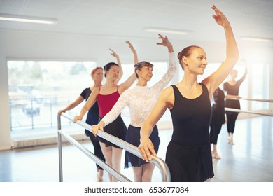 Smiling mature group of ballet performers standing and dancing with hands up in the class.