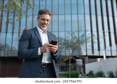 Smiling mature hispanic senior business man using smartphone cellphone at office building. Latin middle age male entrepreneur businessman holding mobile cell phone for trading outdoors. Copy space