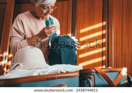 A smiling mature lady packs her suitcase for the trip to Paris to see the Olympics. Happy old woman in bedroom excited for the trip organizes her luggage essential for stay in hotel