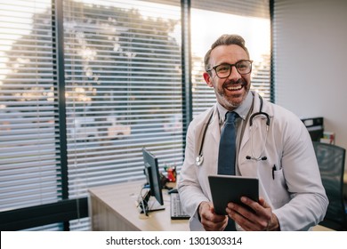 Smiling mature male doctor with digital tablet in his office. Friendly medical professional with tablet computer in clinic.