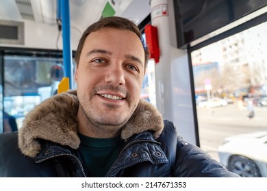 Smiling Mature Man Sitting By Window In Bus During His Morning Commute Looking At Camera. Happy Millennial Man Looking At Camera With Smile, Dressed In Trendy Winter Clothes, Getting To Work By Tram.