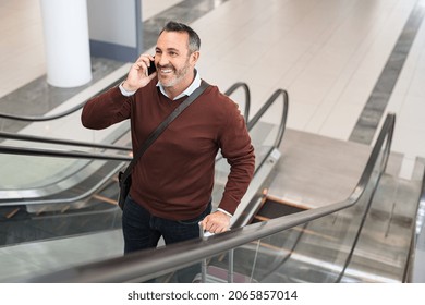 Smiling mature man standing in escalator while talking over smartphone. Successful business man in airport standing on escalator while doing a conversation on the phone. Mid adult man going to work.