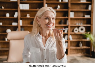 Smiling mature middle-aged businesswoman recording voice message on cellphone while working remotely in office , communicating with colleagues in chat online - Powered by Shutterstock