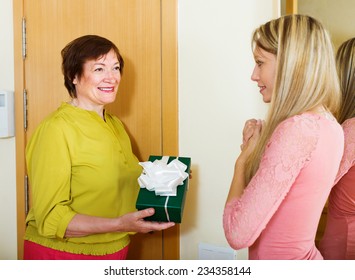 Smiling Mature Neighbor Presenting Gift To Young Girl In Home