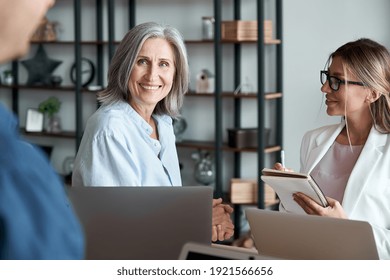 Smiling mature old female mentor coach manager training young interns at group office meeting workshop. Happy middle aged teacher working together with students at class seminar. Mentoring concept. - Powered by Shutterstock