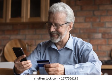 Smiling Mature Old Man In Glasses Enjoying Shopping In Internet Store Using Mobile Phone Applications, Satisfied With Fast Money Transfer Secure Service, Entering Payment Information From Credit Card.