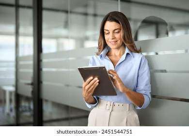 Smiling mature professional business woman using tablet standing in office. Busy middle aged businesswoman manager, older female executive leader holding pad digital tablet at work, looking at pad. - Powered by Shutterstock