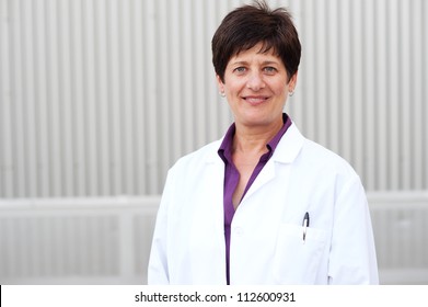 Smiling Mature Professional Woman Dressed In Labcoat Standing Outside