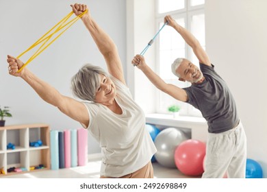 Smiling mature senior man and woman doing stretching exercises with rubber band standing in gym. Happy elderly people doing workout in rehabilitation center for health. Sport and fitness concept. - Powered by Shutterstock