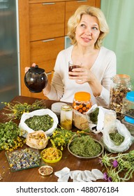 Smiling Mature Woman With Dried Herbs Brewing Herbal Tea At Home  
