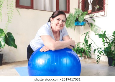 Smiling mature woman exercising at home with a stability ball, embracing a healthy and active lifestyle. Perfect representation of fitness, wellness, and self-care for older adults. - Powered by Shutterstock