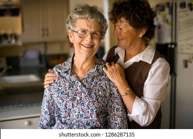 Smiling Mature Woman Gives Her Elderly Mother An Affectionate Squeeze.